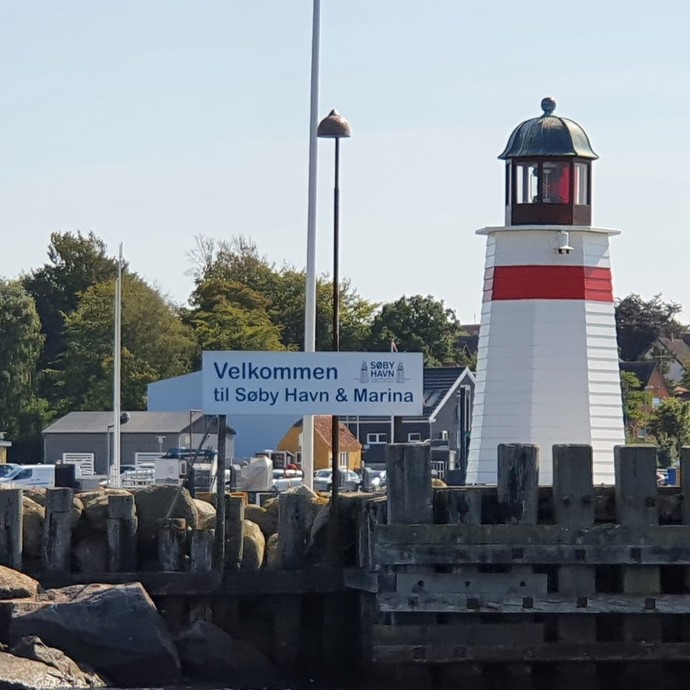 Ein kleiner, rot-weißer Leuchtturm an einer Hafeneinfahrt (vergrößerte Bildansicht wird geöffnet)