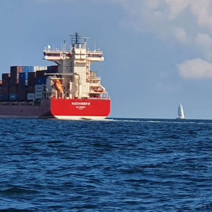 Ein großes Containerschiff neben einem kleinen Segelboot (vergrößerte Bildansicht wird geöffnet)