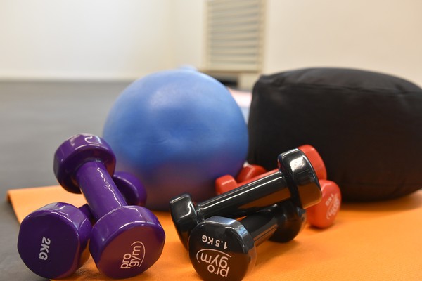 Auf einer orangenen Sportmatte liegen farbige Hanteln, ein Ball und ein Yogakissen
