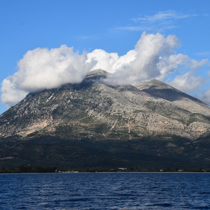 Blick vom Meer auf einen Berg um dessen spitze Wolken kreisen (vergrößerte Bildansicht wird geöffnet)