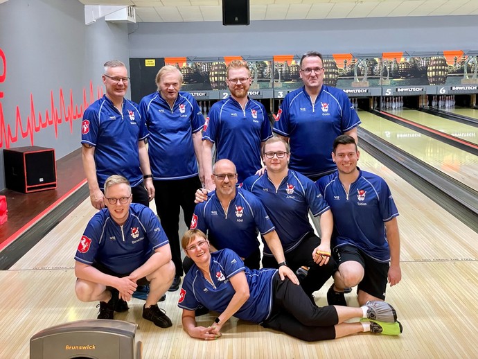 Zehn Personen in blauen Bowlingsshirts stehen auf einer Bowlingbahn
